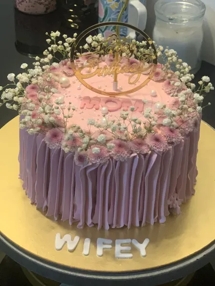 A beautiful pink cake decorated with fresh baby's breath and chrysanthemums. The delicate floral design is perfect for celebrating a mom or wife.
