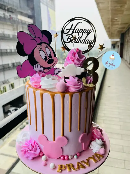A sweet and classic Minnie Mouse drip cake for a third birthday. This pink cake features a golden drip, pink rosettes, and an adorable baby Minnie Mouse topper.