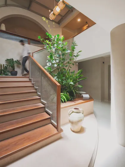 The entryway of this home is designed around a central staircase and a planter bed, reminiscent of a traditional courtyard. The wooden archway frames the view, creating a layered and welcoming first impression.
