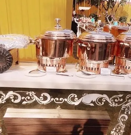 A detailed view of our buffet counter with intricate white vinyl work. The setup includes our signature copper chafing dishes and a unique shell-shaped serving platter.