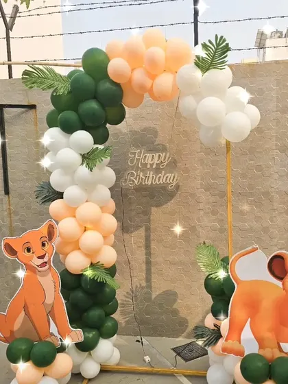 A Lion King "Simba" themed birthday decoration for an outdoor party, using a balloon arch in jungle colors and character cutouts.