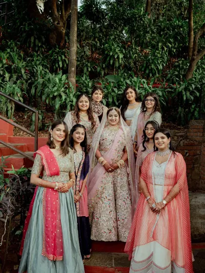 The bride poses with her bridesmaids on a staircase surrounded by lush greenery. A beautiful group portrait capturing the friendship and support of her bride tribe.