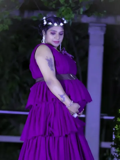 A serene nighttime maternity portrait of a woman in a purple ruffled gown, gently cradling her baby bump.