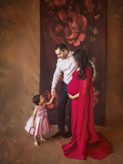 A candid moment where parents interact with their young daughter during a studio maternity shoot. The image feels natural and full of affection, set against an artistic backdrop.