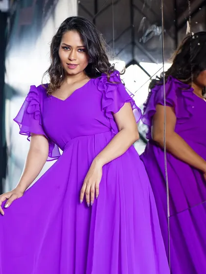A close-up of the purple gown, showing the delicate flutter sleeves and the soft drape of the fabric.