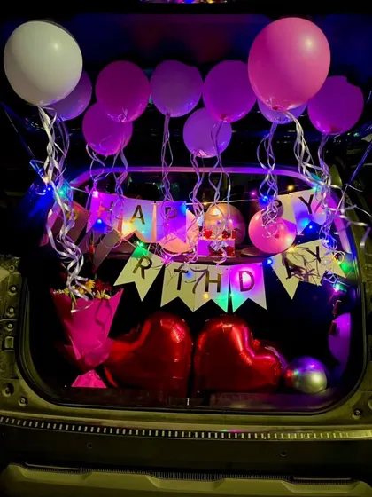 A complete car boot decoration with a "Happy Birthday" banner, heart-shaped foil balloons, a bouquet, and colorful lights. I can customize the colors and elements for you.