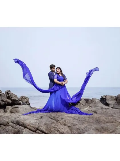 A dramatic "flying gown" shot on the rocks. The blue trail creates a beautiful wing-like shape against the sky, perfect for a statement pre-wedding photo.