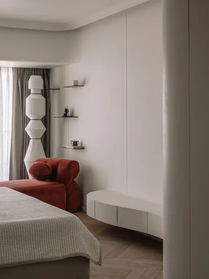 A corner of the master bedroom, showing the interplay of the rust-colored chaise, the totem-like floor lamp, and the soft, neutral tones of the room.