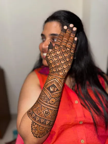 A happy bride showcasing her stunning back-of-hand mehendi. The design features a classic grid pattern, which is a timeless and elegant choice.