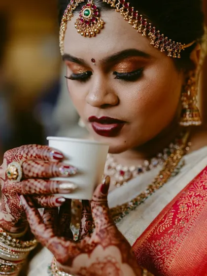 A close-up of a bride's hands, adorned with henna and rings, as she sips her coffee. A beautiful detail shot.