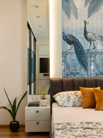 A bedroom that exudes personality, with a stunning peacock-themed wallpaper behind a dark grey upholstered bed. Mirrored panels on either side add a touch of glamour.