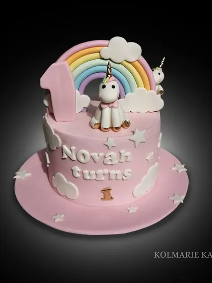 A magical unicorn and rainbow cake for a first birthday. This pink cake is decorated with fondant clouds, stars, and a cute unicorn sitting under a pastel rainbow.