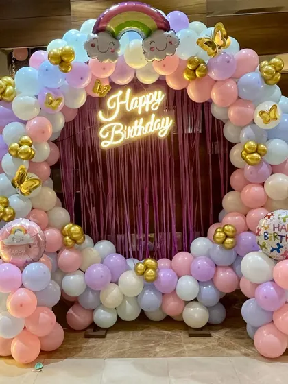 A beautiful pastel-colored balloon ring with a 'Happy Birthday' neon sign and a purple fringe curtain, perfect for a unicorn or princess party.