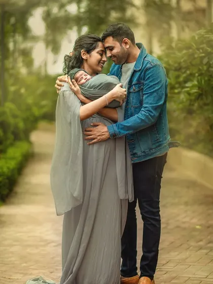 A new mother and father touch foreheads as they lovingly cradle their newborn baby between them. This intimate outdoor portrait is filled with emotion and the magic of new parenthood.