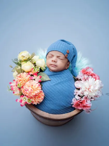 A beautifully simple newborn portrait. The baby is swaddled in blue and placed in a basket adorned with flowers, creating a serene and artistic image against a matching blue background.