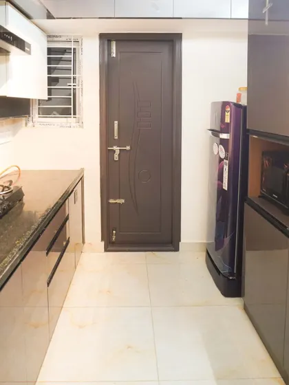 A view of a parallel kitchen layout, featuring glossy beige cabinets and a dark countertop. The design includes a tall unit for an integrated microwave and refrigerator, demonstrating efficient space planning for a modern apartment.