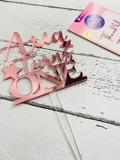 Here is the "Aria Turns ONE" topper in rose gold, laid flat to show the precise cut and design details before it goes on the cake.