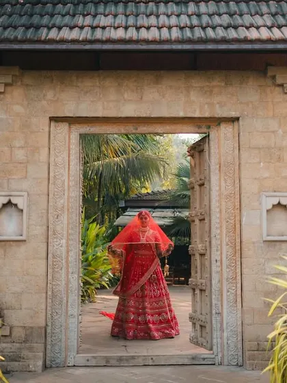 The bride, a vision in red, stands framed by an ancient stone archway, her veil adding an element of mystery and timeless beauty.