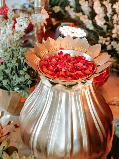 The warm glow of lights reflecting on the brass lotus urn, adding to the rich and inviting ambiance of the traditional event.