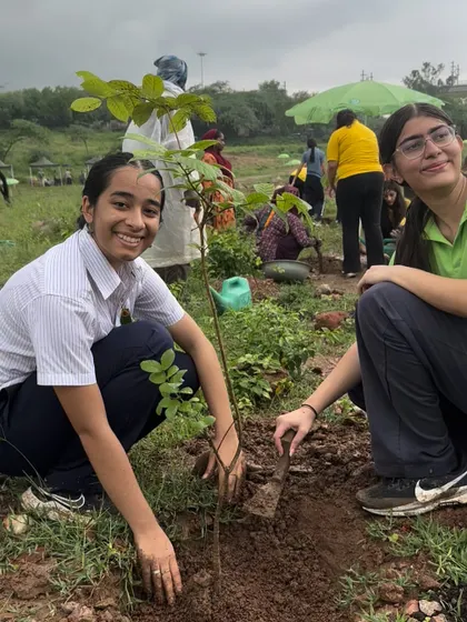 Two smiling students pose with the large native sapling they just planted, proud of their contribution to restoring Gurgaon's green cover.