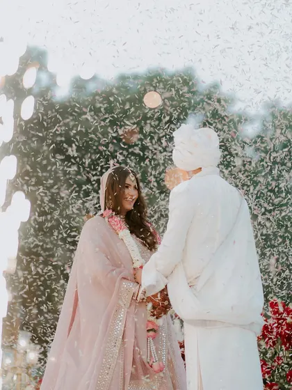 A joyous moment captured amidst a shower of petals. The green foliage backdrop provides a fresh, natural contrast to the couple's festive attire.