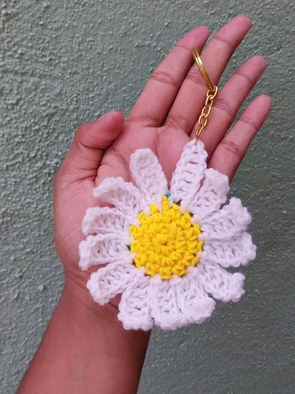 The full-sized crochet daisy keychain, held in hand. It's a cheerful and bright addition to any set of keys.