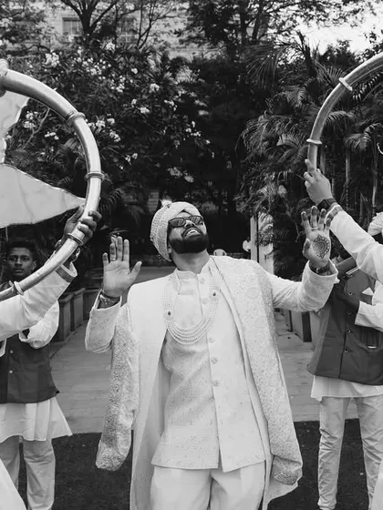 A celebratory black and white shot of the groom, Apurva, during his baraat, welcomed by traditional horn players.