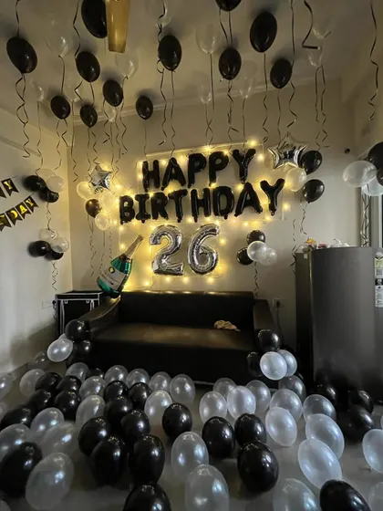 A full room decoration for a 26th birthday. The setup includes black and silver balloons on the floor and ceiling, 'Happy Birthday' foil letters, and a champagne balloon.