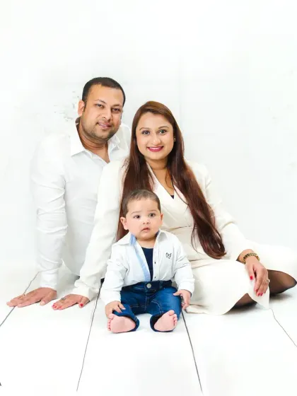 A classic family photo with both parents and their baby seated together, smiling warmly. The all-white theme creates a timeless and elegant look.