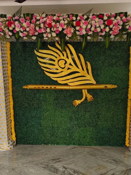 A close-up of the Krishna feather and flute motif against a green grass backdrop. This is a popular and auspicious theme for traditional naming ceremonies.