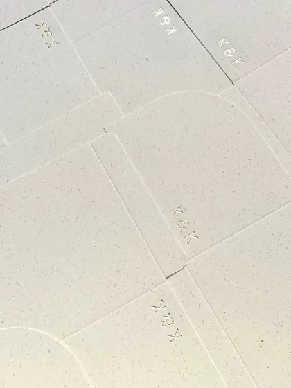 A sheet of textured, handmade paper with the 'K&K' monogram subtly debossed. The texture of the paper itself adds a layer of understated luxury.
