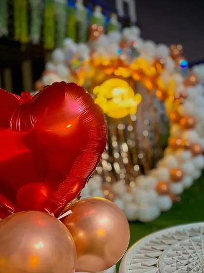 A close-up of the outdoor romantic setup, focusing on the heart-shaped foil balloon and the elegant rose gold and white balloon arch in the background.
