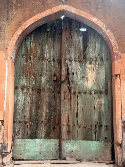 A weathered green wooden door with metal studs, showing its age and resilience. We discuss the materials and techniques used to build these structures that have stood for centuries.