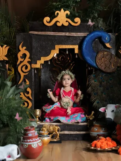 Our little Radha sitting on her throne in a lush, green Vrindavan-inspired set. We pay attention to every detail, from the peacock decor to the little matkas.