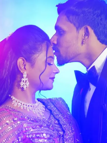A romantic shot of the groom kissing his bride's forehead, with beautiful blue and purple lighting creating a dreamy reception atmosphere.