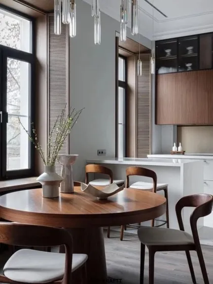 This wide shot shows the kitchen's integration with the dining area, where a round wooden table and chairs complement the natural tones of the kitchen cabinetry.