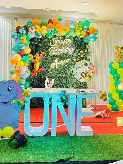 A jungle-themed first birthday with a green foliage backdrop and a "ONE" table. The decor is accented with an elephant cutout and a light-up number '1'.