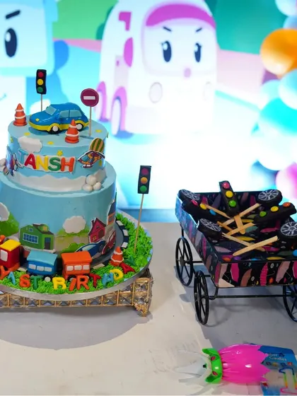 A closer look at the details of a transportation-themed party. The custom cake and a cart filled with themed return gifts add a special touch to the celebration.