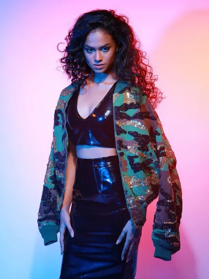 A powerful stance from the Diseno.in model, highlighting the contrast between the tough camo jacket and the sleek vinyl outfit.