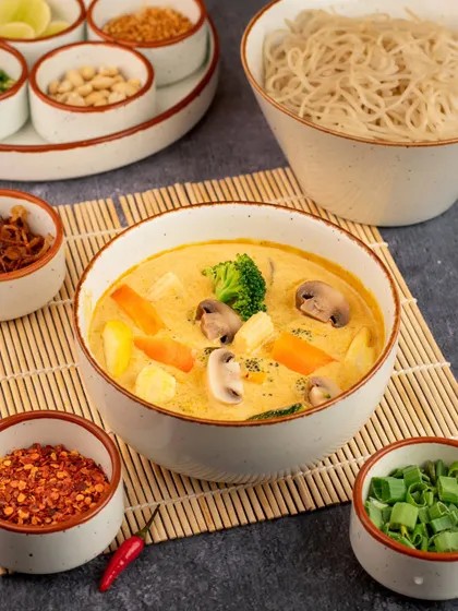 We brought this Burmese Khao Suey to life by showcasing all its delicious components. The main bowl is surrounded by various condiments, inviting the viewer to imagine customizing their own meal.