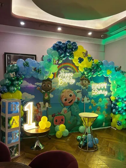 A Cocomelon-themed first birthday party with a neon green and blue color scheme. The setup includes a custom backdrop, 'BABY' blocks, and a neon sign.