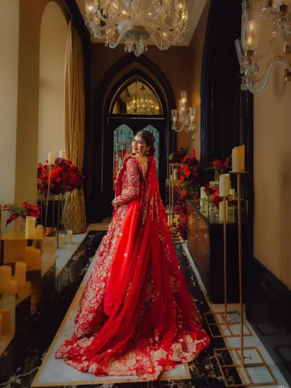 A stunning shot of the bride from the back, her long red veil trailing behind her as she walks down a candle-lit corridor.