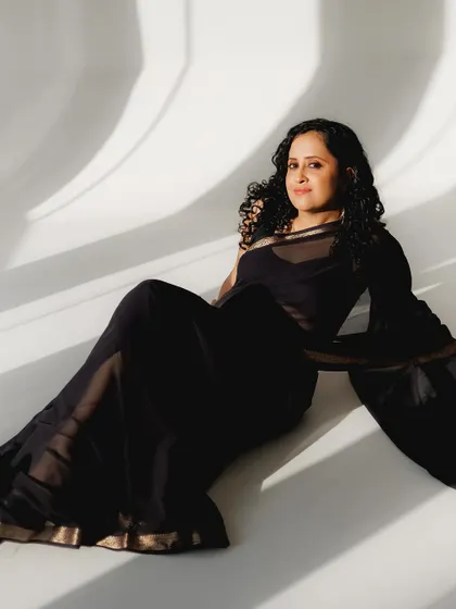A full-length shot from a modern photoshoot. The client is wearing a simple black saree, and her natural curls and subtle makeup create a look of effortless elegance.