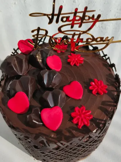 An indulgent chocolate cake decorated with a chocolate cage, chocolate hearts, and red fondant details.