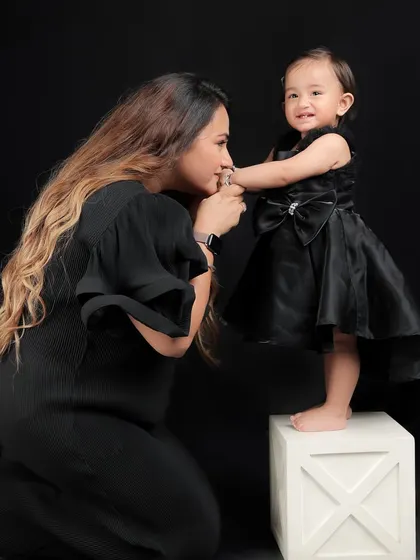 A mother's gentle kiss for her daughter's hand. This tender moment, captured against a dramatic black backdrop, is timeless and elegant.