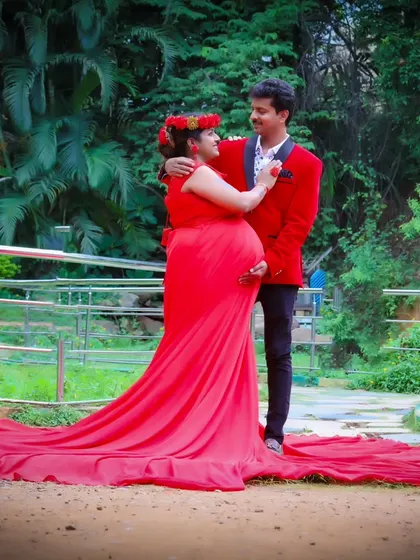 A beautiful outdoor maternity shoot with the couple in red. The woman's long trail gown spreads out elegantly on the grass.