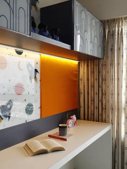 A close-up of a kids' study area with a long desk and overhead cabinets. The design includes a fun, space-themed whiteboard and pinboard, making it a practical and inspiring spot for learning.