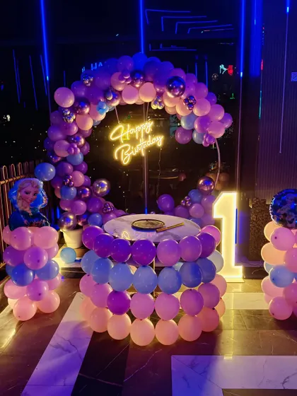 A Frozen-themed first birthday with a round balloon-wrapped table and a neon 'Happy Birthday' sign.