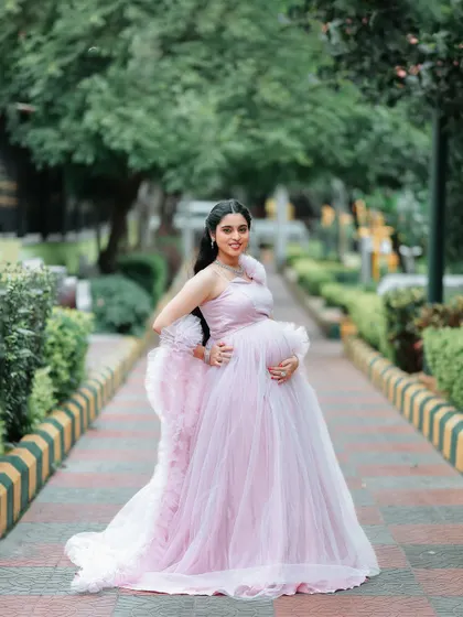 A side profile view that beautifully showcases the baby bump. The ruffled detailing on the gown adds texture and volume, creating a very feminine silhouette.
