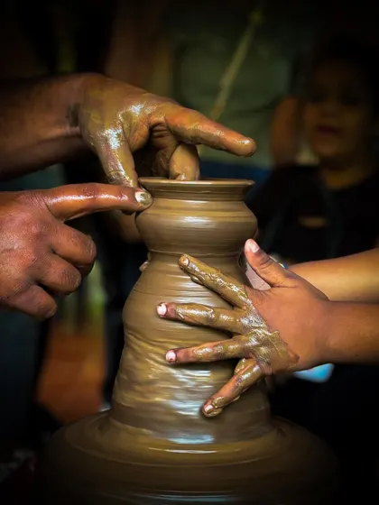 A close-up view of hands working together on the pottery wheel. This activity is a wonderful way for parents and children to connect and create a shared memory.